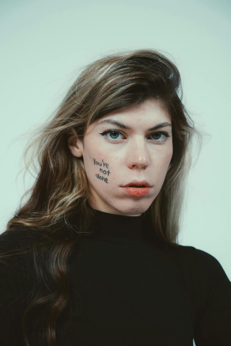 Close-up portrait of a person with 'You're Not Alone' written on their cheek.